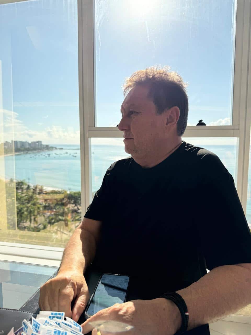 Sr. Ivan, fundador da IRLog, sentado à mesa com vista para o mar, representando experiência, visão estratégica e liderança no setor logístico