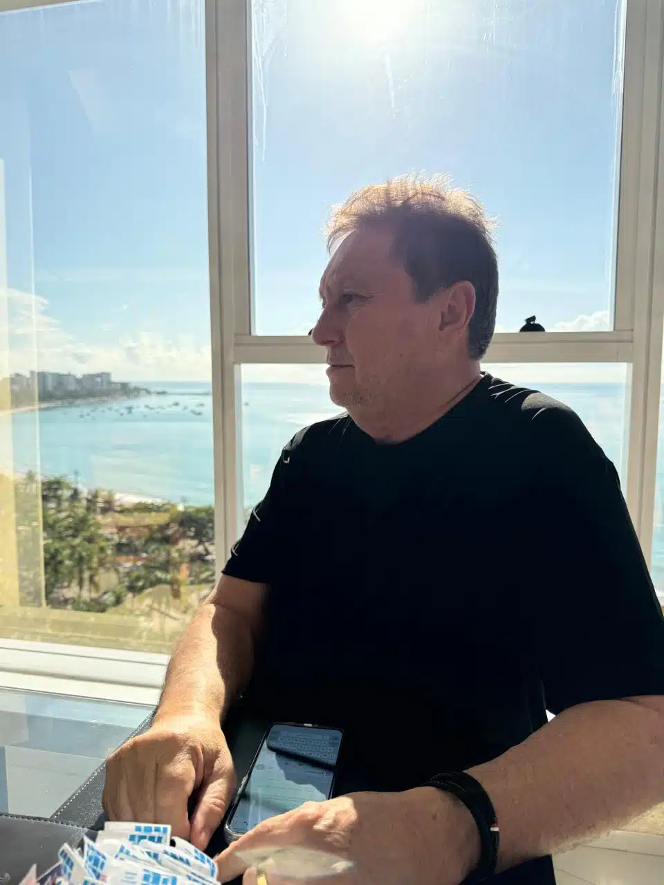 Sr. Ivan, fundador da IRLog, sentado à mesa com vista para o mar, representando experiência, visão estratégica e liderança no setor logístico